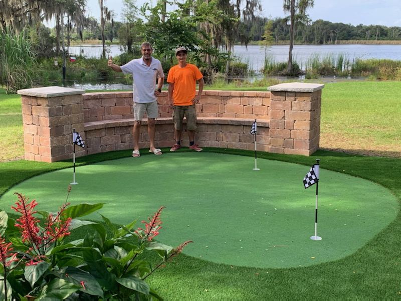 Two men standing behind a finished backyard putting green at a lakefront home