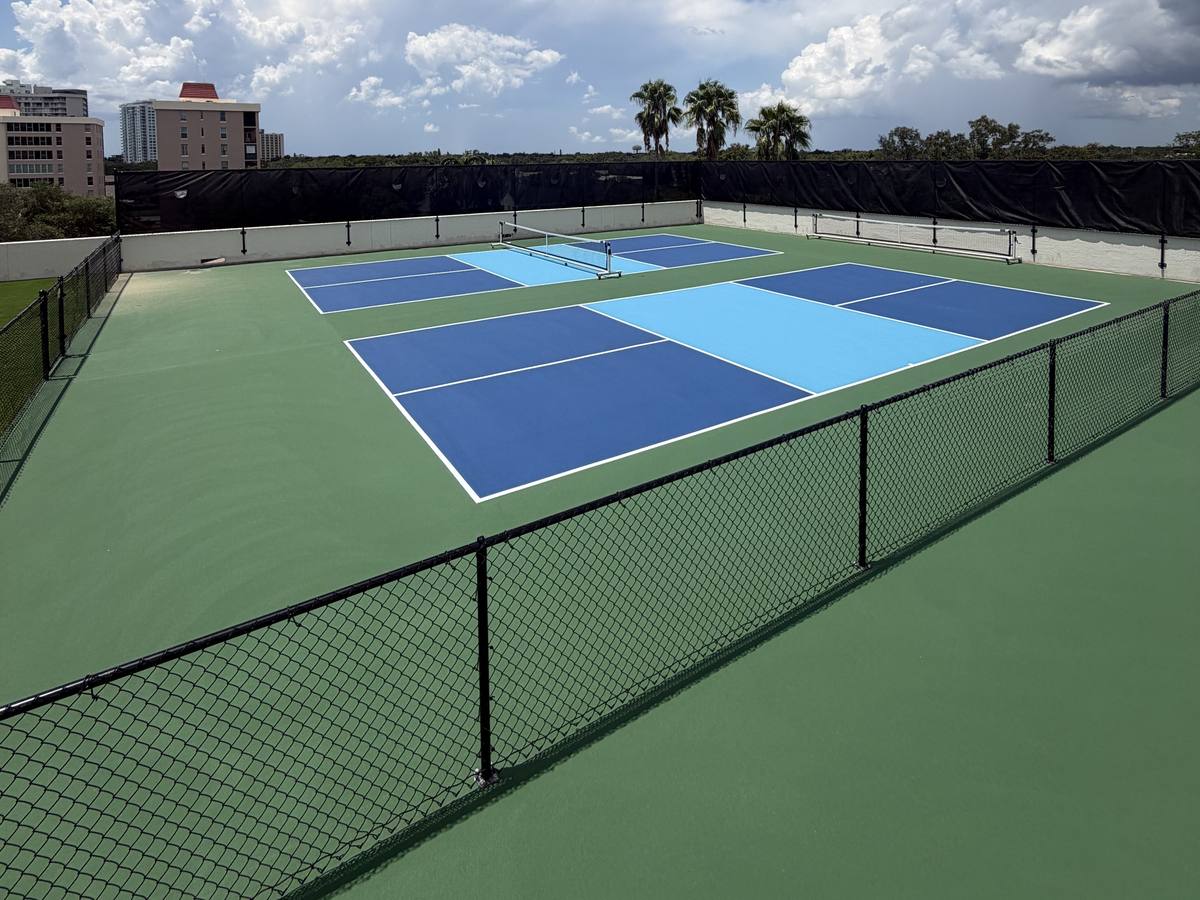 Two rooftop pickleball courts in two-tone blue with black fencing and the Tampa skyline behind