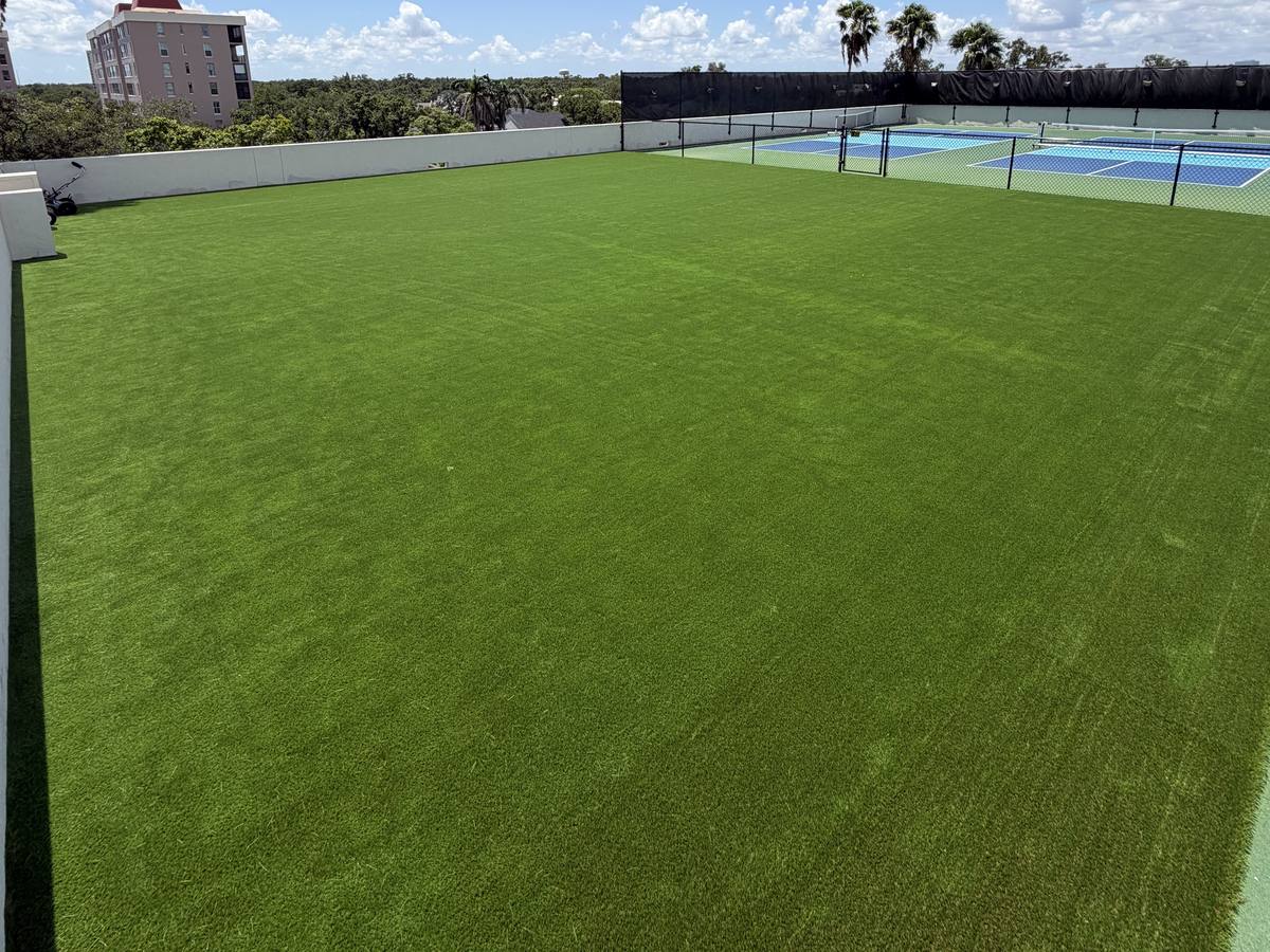Large rooftop turf field with fenced two-tone blue courts at the far end