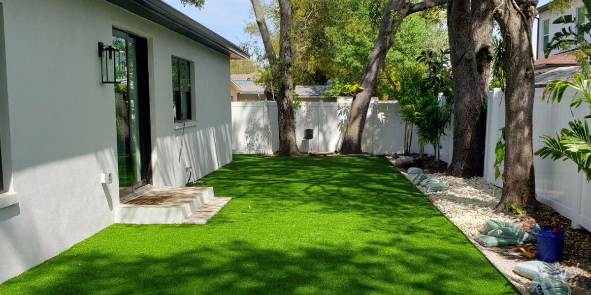 Shaded side yard finished in synthetic turf along a white vinyl fence