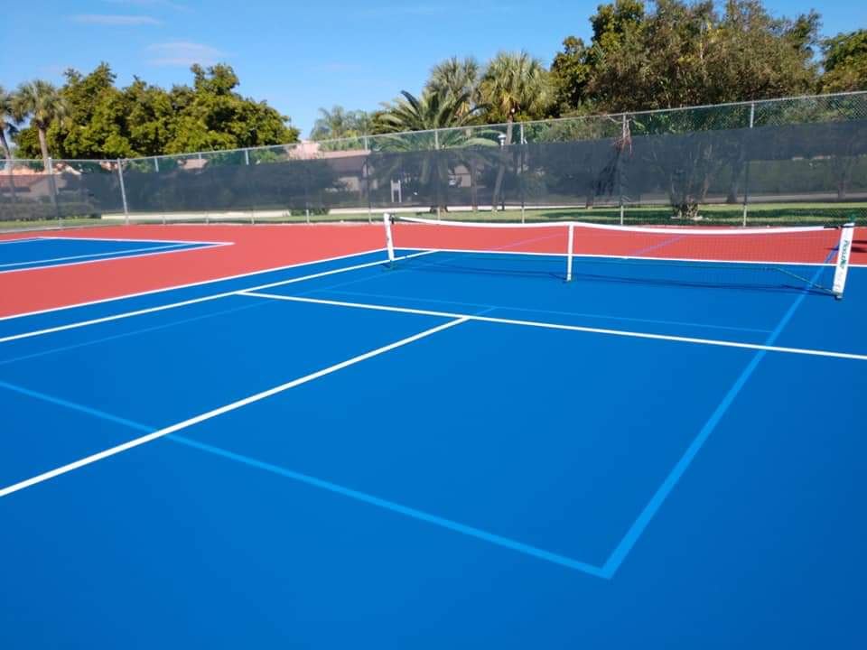 Pickleball court in red and blue with a net, fenced and lit