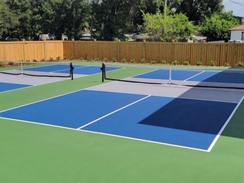 Two side‑by‑side pickleball courts in blue and green with a wood fence