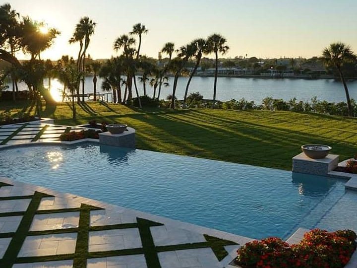 Sunset over an infinity pool with a turf-ribbon tile deck and palm trees