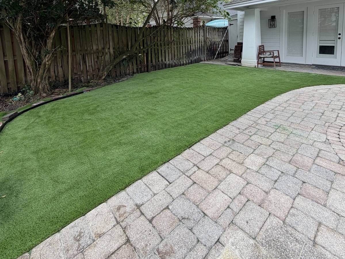 Pet turf curving into a paver patio beside a white house