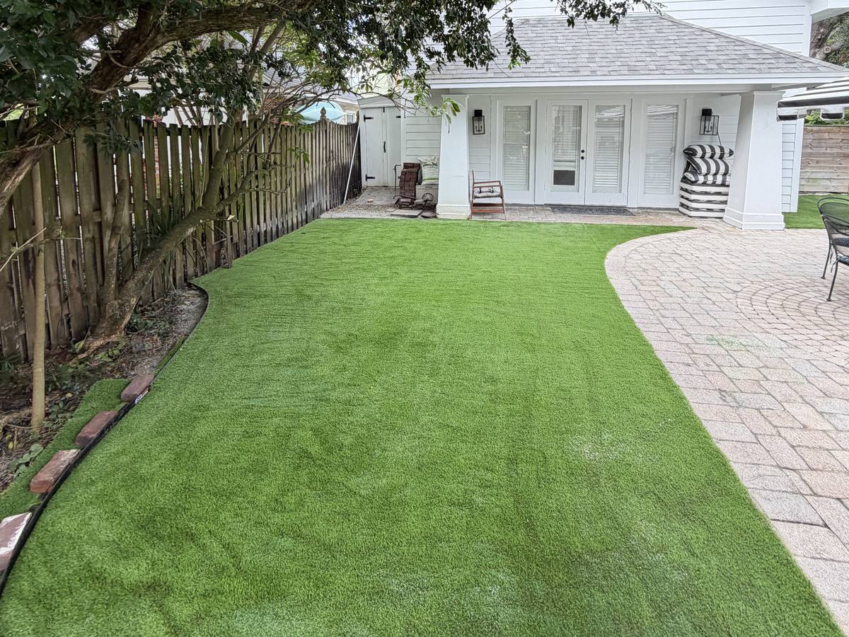 Backyard pet turf meeting a paver path behind a white house