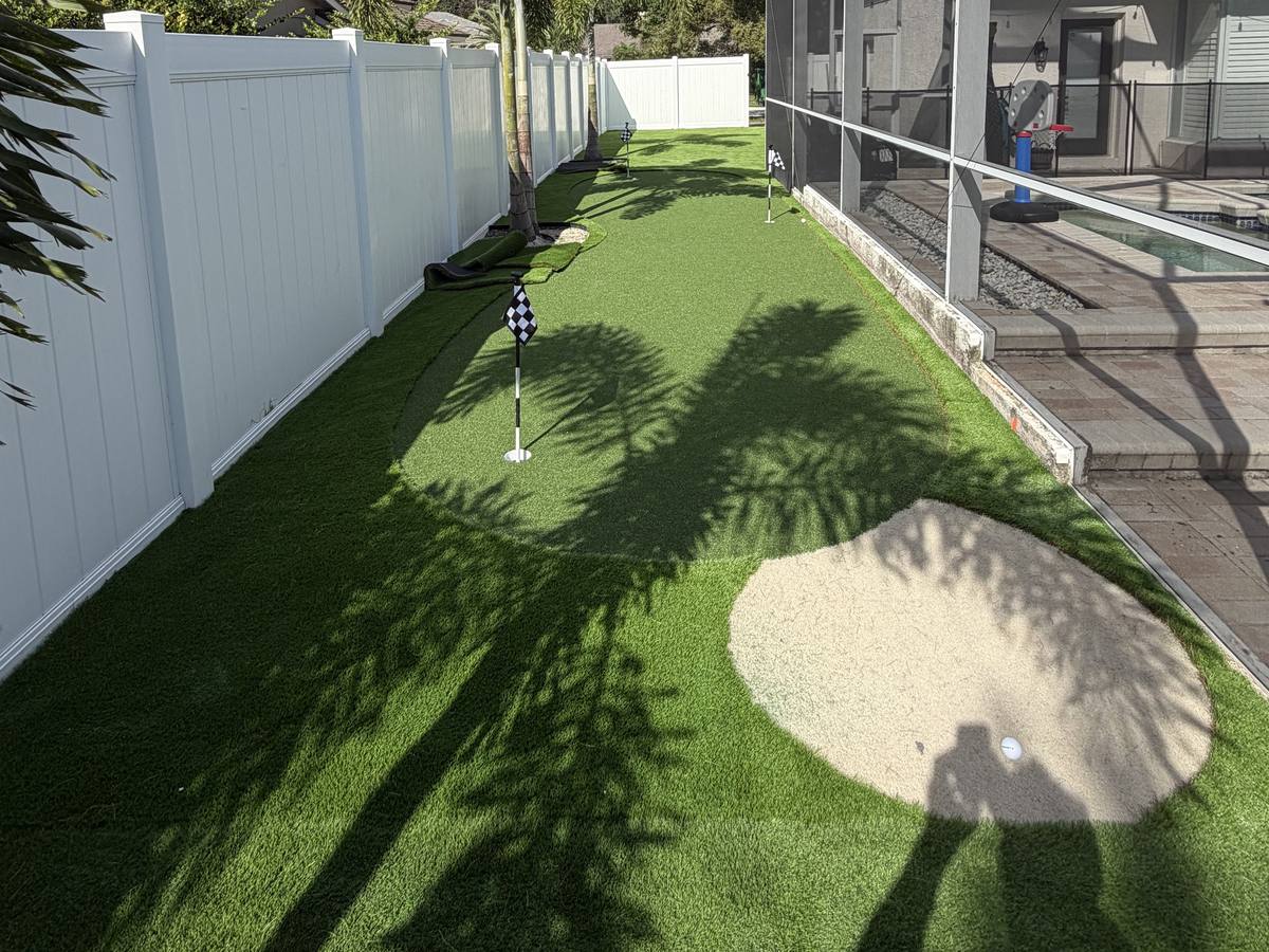 Putting green with a sand bunker along a white vinyl fence