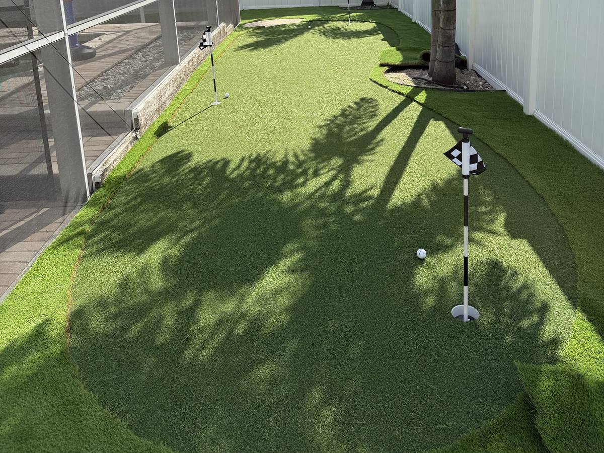 Putting green with three cups and a checkered flag beside a screened lanai